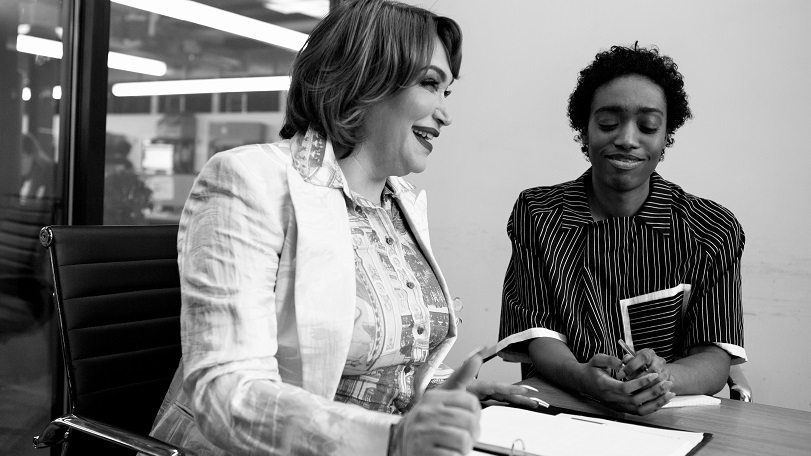 Due persone che lavorano insieme: una donna transgender e una persona non binaria, sorridono in un meeting di lavoro. La foto è in bianco e nero